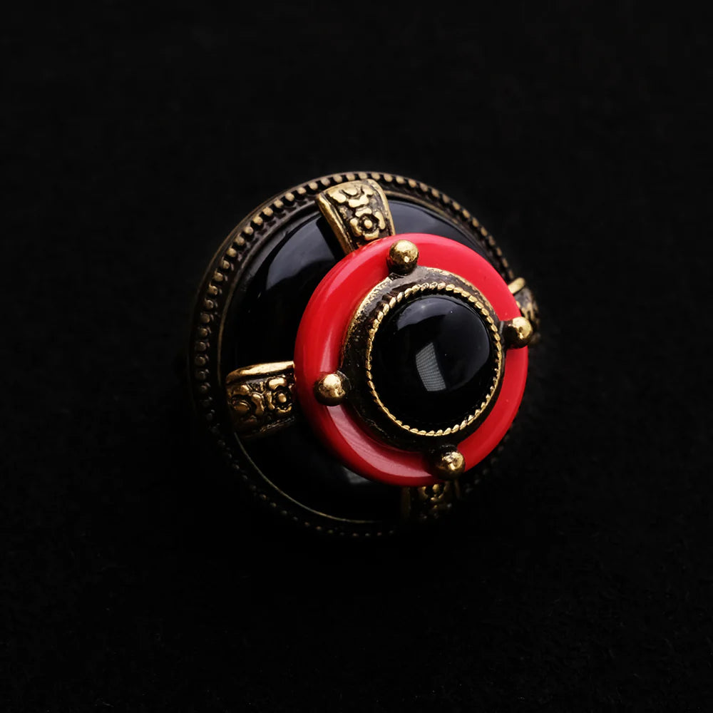Bague en agate noire et rouge, style ancien, avec des détails dorés et un design circulaire complexe, sur fond noir.