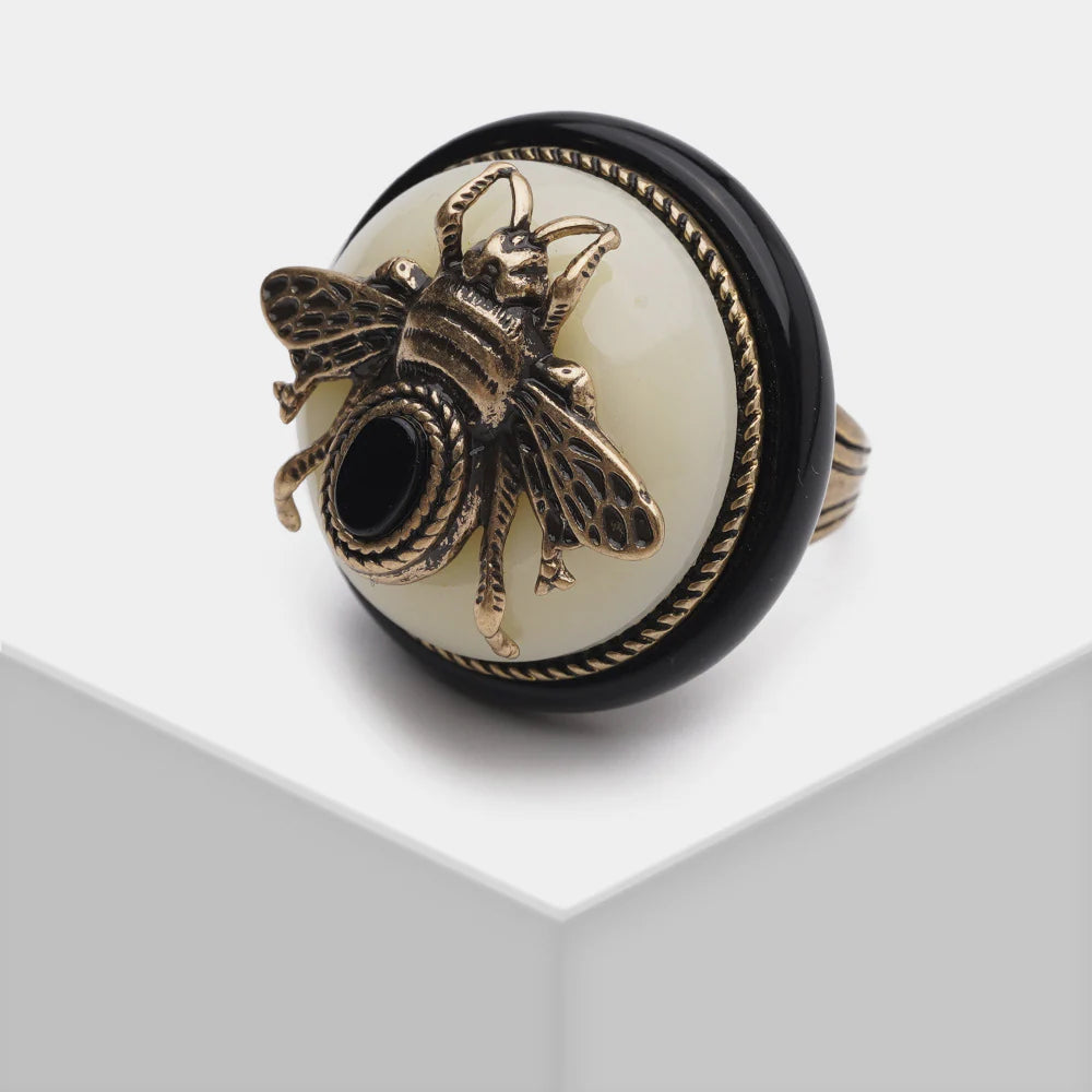 Bague "Reine Noire" avec une abeille en métal doré sur une agate noire et une pierre blanche, bordure torsadée noire.