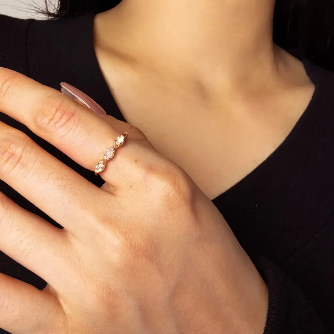 Bague fine en argent doré à l'or, ornée de trois petites pierres claires, dont une opale, portée au doigt.
