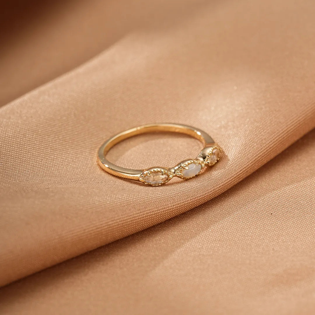 Bague alliance lumineuse en argent doré or avec trois opales marquises délicatement serties sur un fond satiné beige.