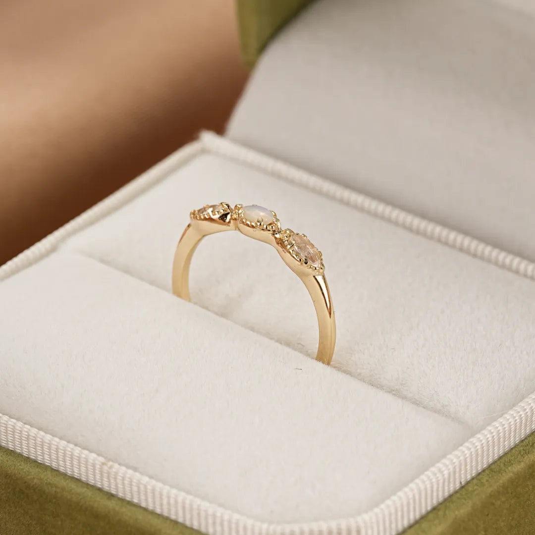 Bague Alliance Lumineuse en argent doré or sertie d'une opale centrale et de deux pierres de lune ovales, posée dans un écrin vert.