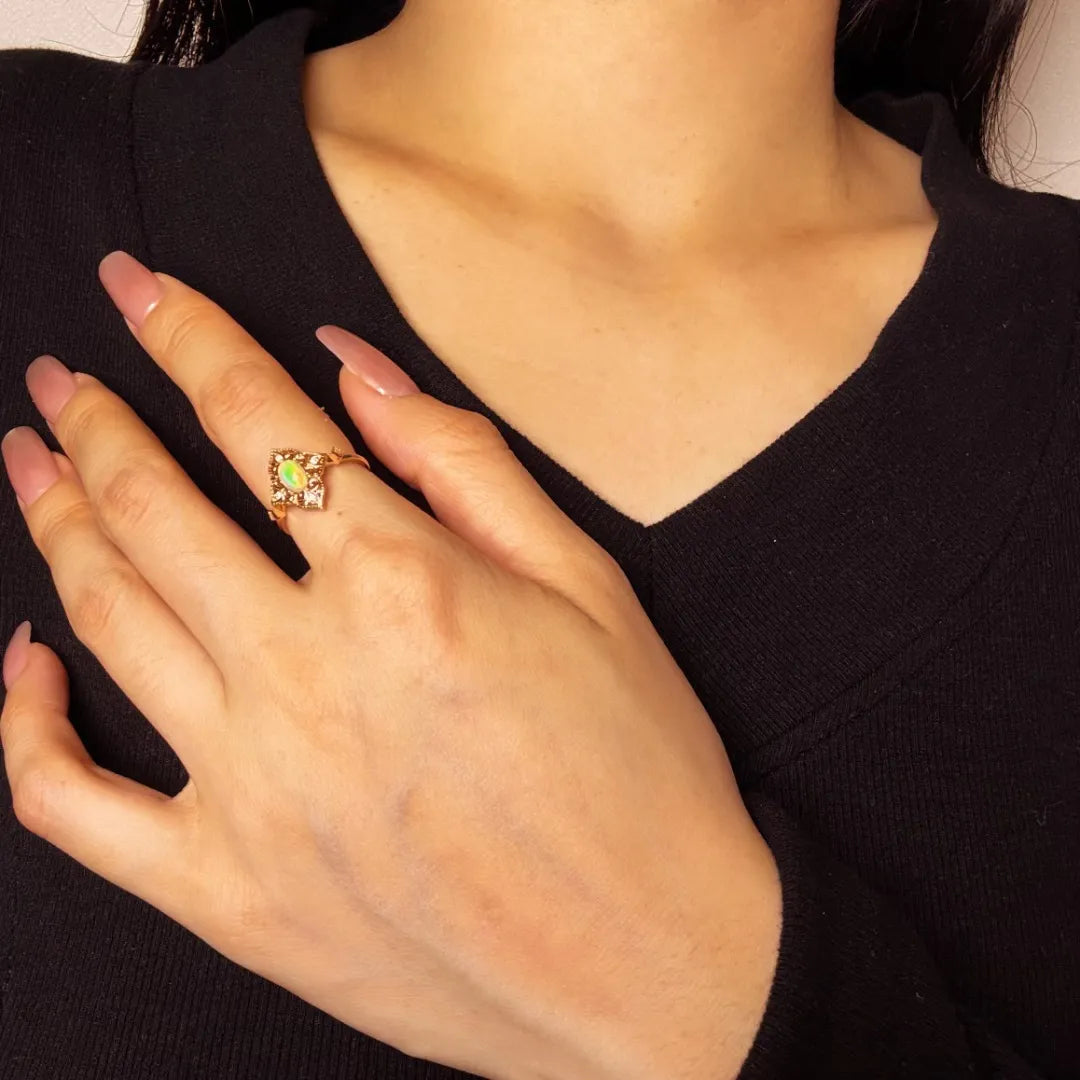 Bague en argent doré à l'or 10K avec une opale centrale de forme carrée et des détails ciselés sur le côté. La bague est portée à l'annulaire d'une main.
