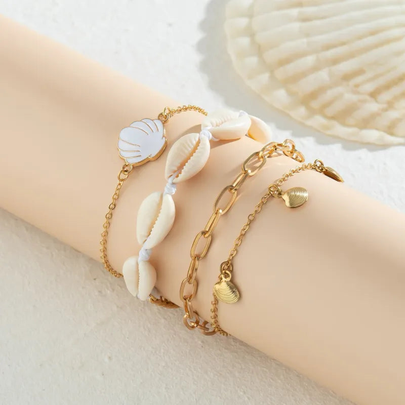 Ensemble de trois bracelets de cheville dorés ornés de coquillages naturels et d'un coquillage blanc émaillé, parfaits pour un look estival.