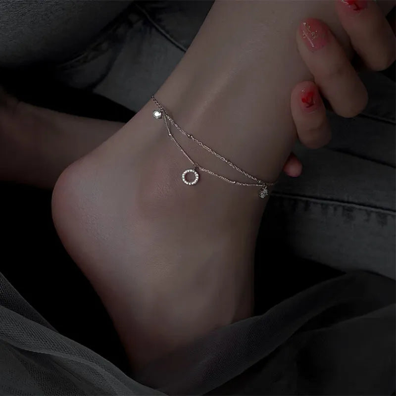 Bracelet de cheville double chaîne en argent avec un pendentif rond serti de zircons et une petite pierre scintillante.