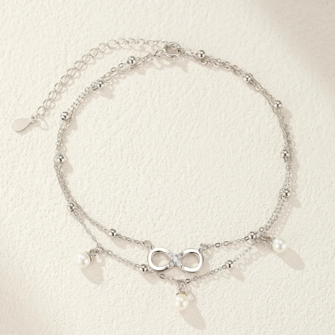 Bracelet de cheville double chaîne en argent 925 avec un pendentif signe infini serti de zircons et orné de perles nacrées.