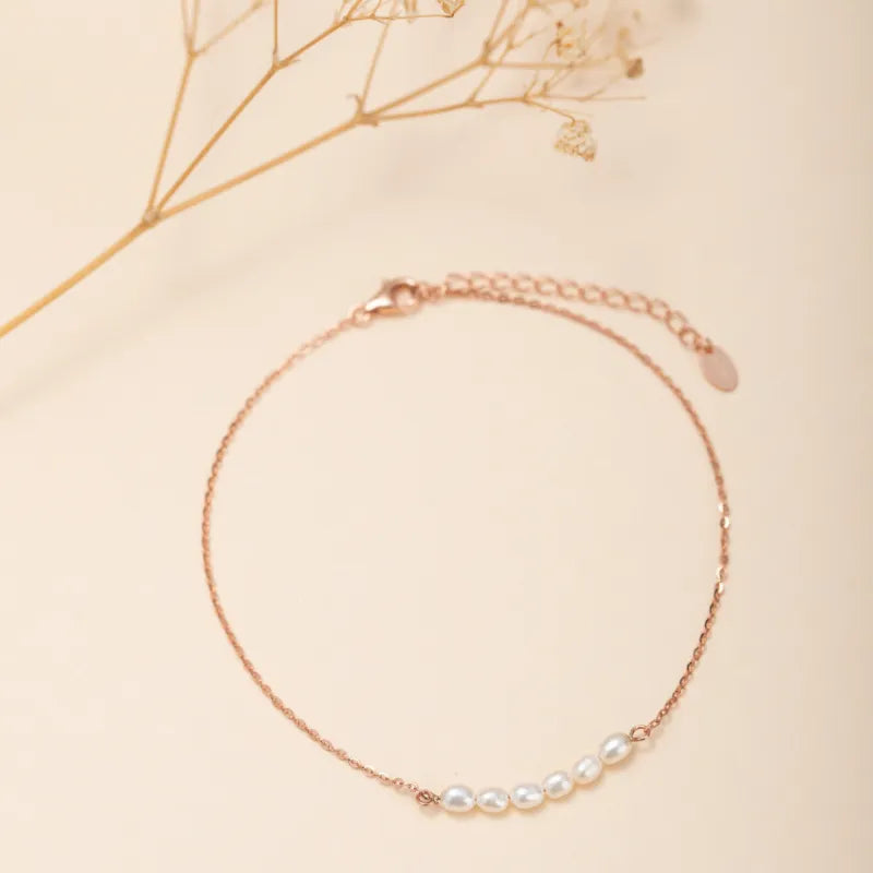 Bracelet de cheville en argent rose avec une fine chaîne et une série de sept petites perles blanches disposées le long de la chaîne.