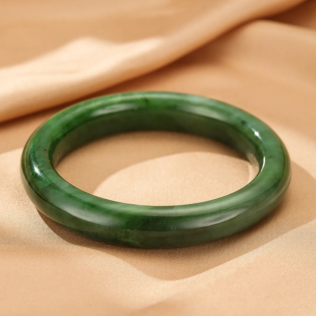 Bracelet jonc en jade naturel "Verdure Éternelle", bijou vert profond et lisse, posé sur un fond satiné beige.