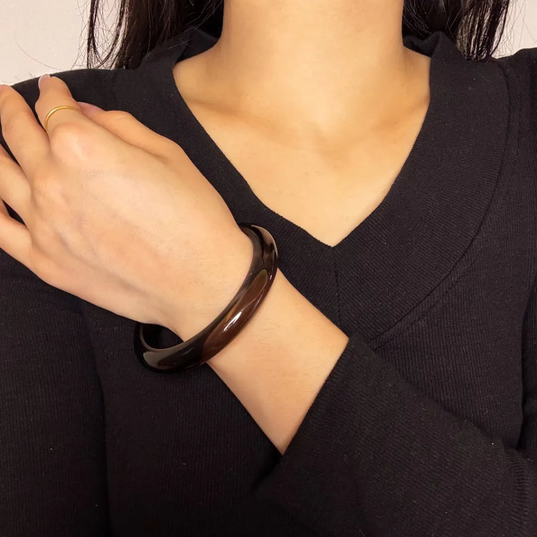 Bracelet jonc en obsidienne au ton brun foncé porté au poignet d'une femme avec un pull noir et une bague dorée discrète.