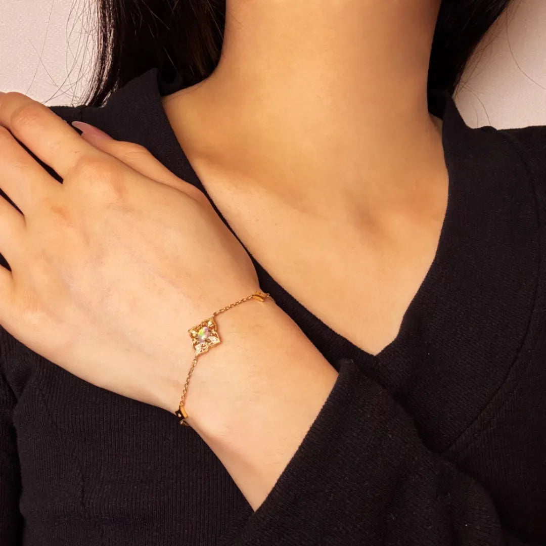 Bracelet fin en argent doré 10K avec un pendentif carré orné d'une opale aux reflets irisés, porté au poignet d'une femme.