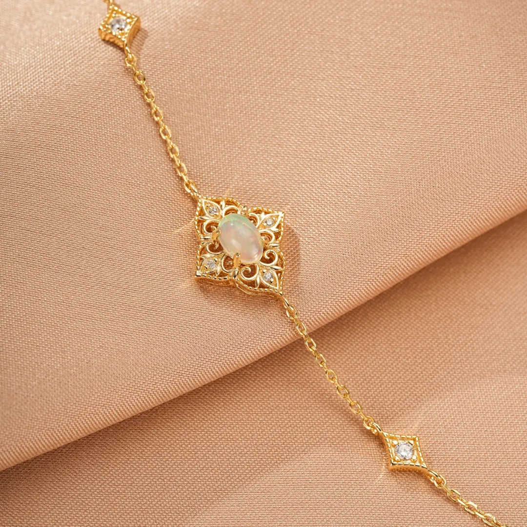 Bracelet en argent doré or 10K avec une opale centrale ovale, entourée de diamants et de motifs ajourés, sur fond de tissu satiné.