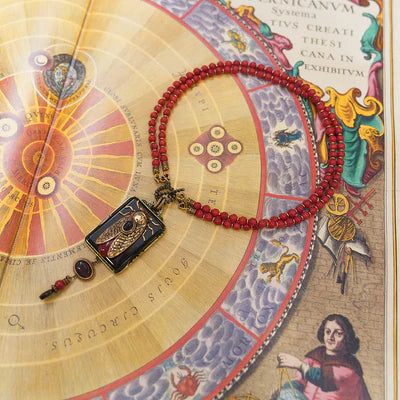 Collier Agate "Beauté Naturelle" avec pendentif rectangulaire noir orné d'une cigale dorée et d'une petite pierre rouge, monté sur un double cordon de perles rouges.