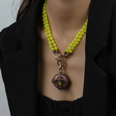 Collier ras de cou avec deux rangées de perles jaune vif et un pendentif rond orné d'une abeille stylisée et d'une pierre verte, porté par un mannequin.