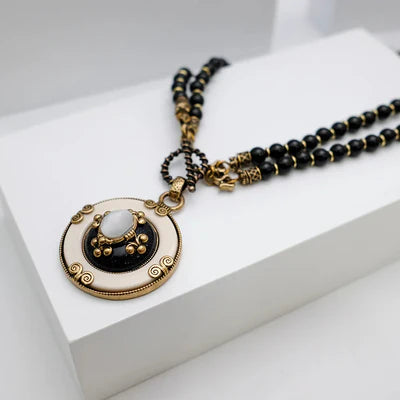 Collier "Pureté Mystique" avec pendentif rond blanc et noir orné d'une pierre centrale ovale et de perles noires.