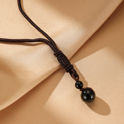 Collier avec une boule d'obsidienne noire et une perle plus petite attachées à un cordon marron réglable avec un nœud tressé.