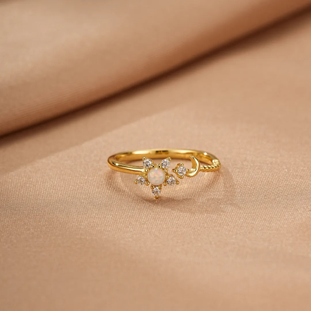 Bague en argent dorée ornée d'une opale centrale entourée de petites pierres scintillantes et d'un croissant de lune.