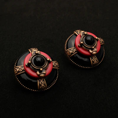 Boucles d'oreilles rondes "Merveille d'Antan" en agate noire, avec un détail rouge corail et un cabochon noir au centre, ornées de motifs dorés sur fond noir.
