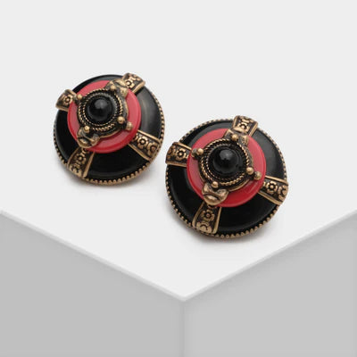 Paire de boucles d'oreilles rondes avec un centre noir et un anneau rouge, ornées de détails dorés et d'une pierre noire au centre.