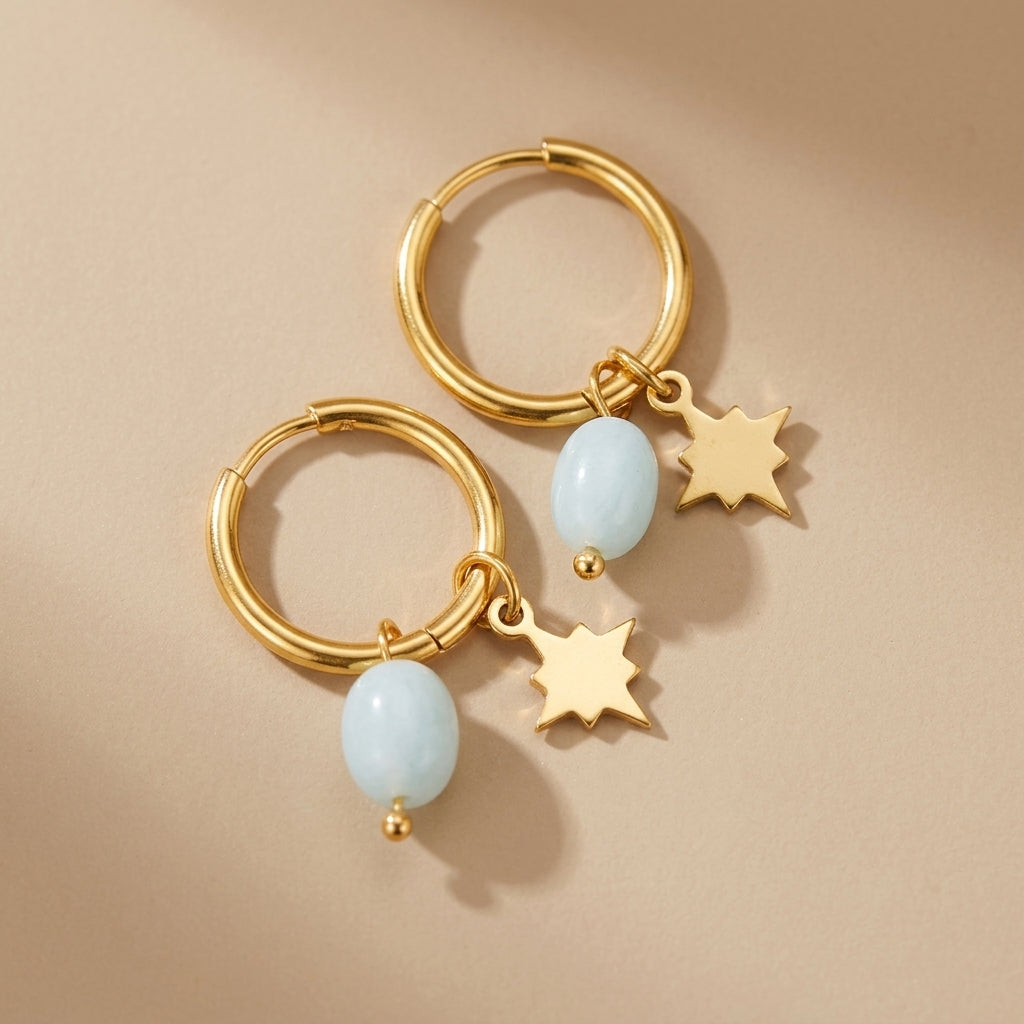 Boucles d'oreilles créoles dorées ornées d'une petite pierre bleu pâle et d'un breloque étoile dorée. @main
