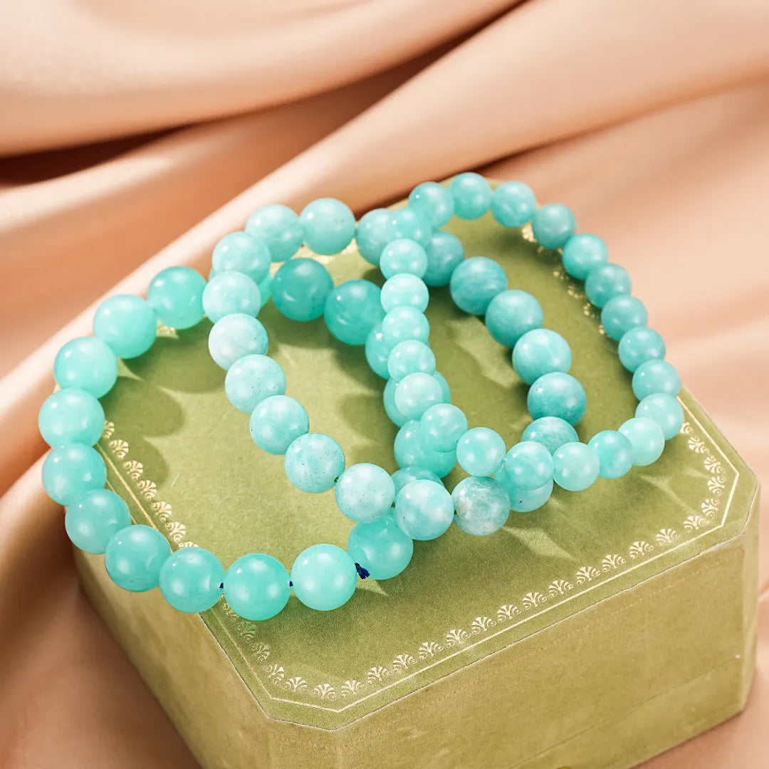 Deux bracelets faits de perles d'amazonite bleu-vert clair reposent sur une boîte verte ornée.