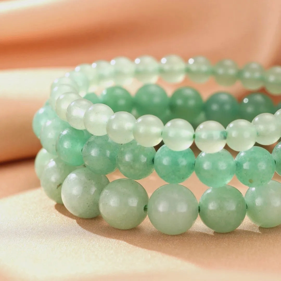 Trois bracelets empilables en aventurine verte, la pierre des pierres de guérison et de sérénité, sur un fond doux et satiné.