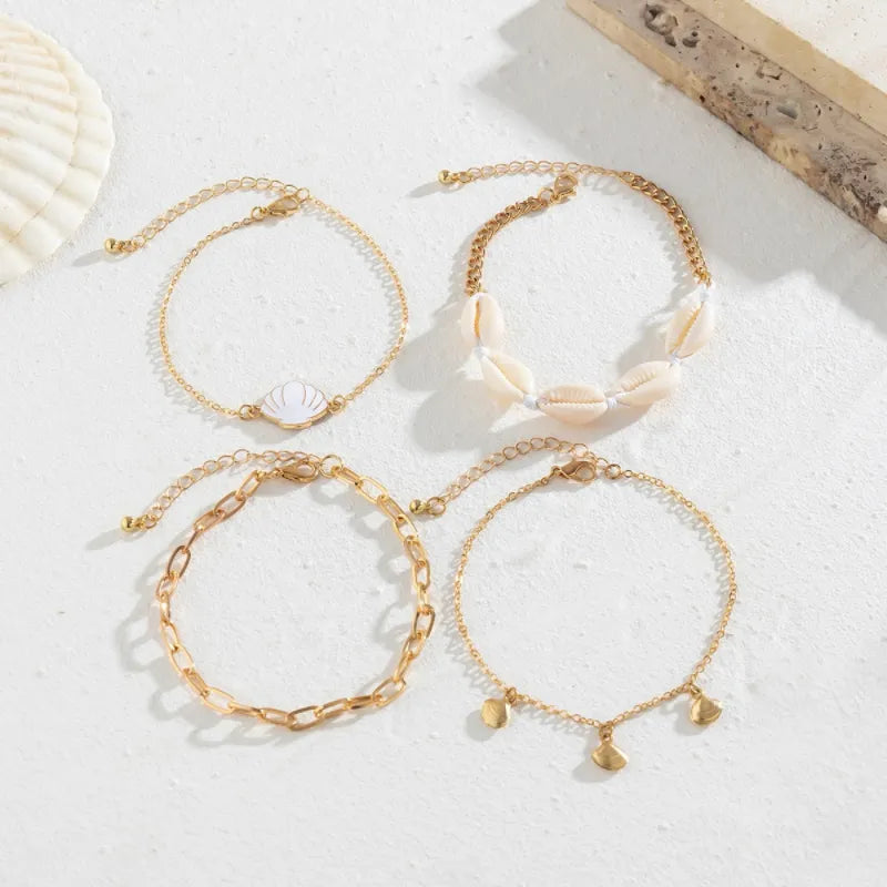 Ensemble de quatre bracelets de cheville dorés, dont un avec un pendentif coquillage blanc, un autre avec des coquillages naturels, un troisième à maillons, et le dernier avec des pendentifs en forme de coquillage.