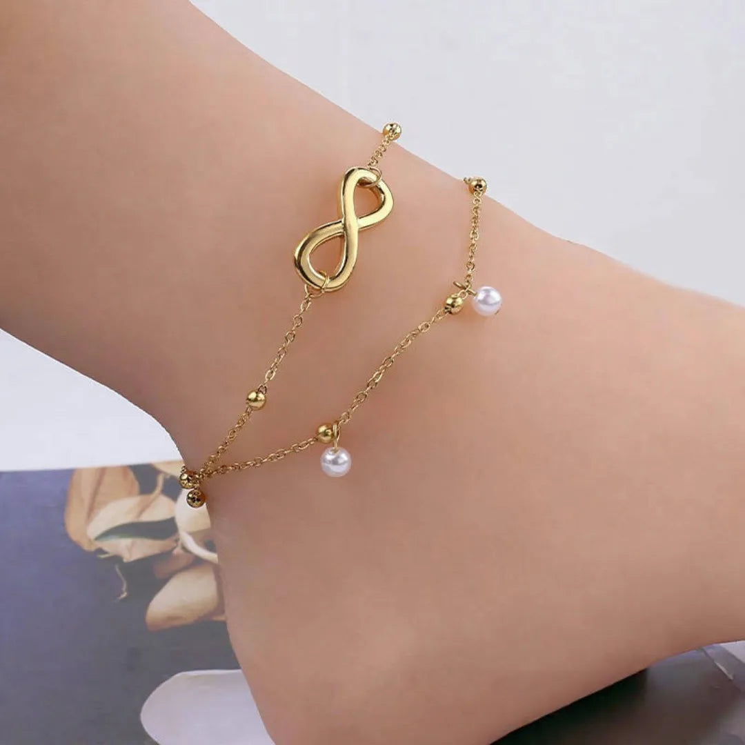 Bracelet de cheville double chaîne en plaqué or avec un symbole infini et de petites perles blanches suspendues.