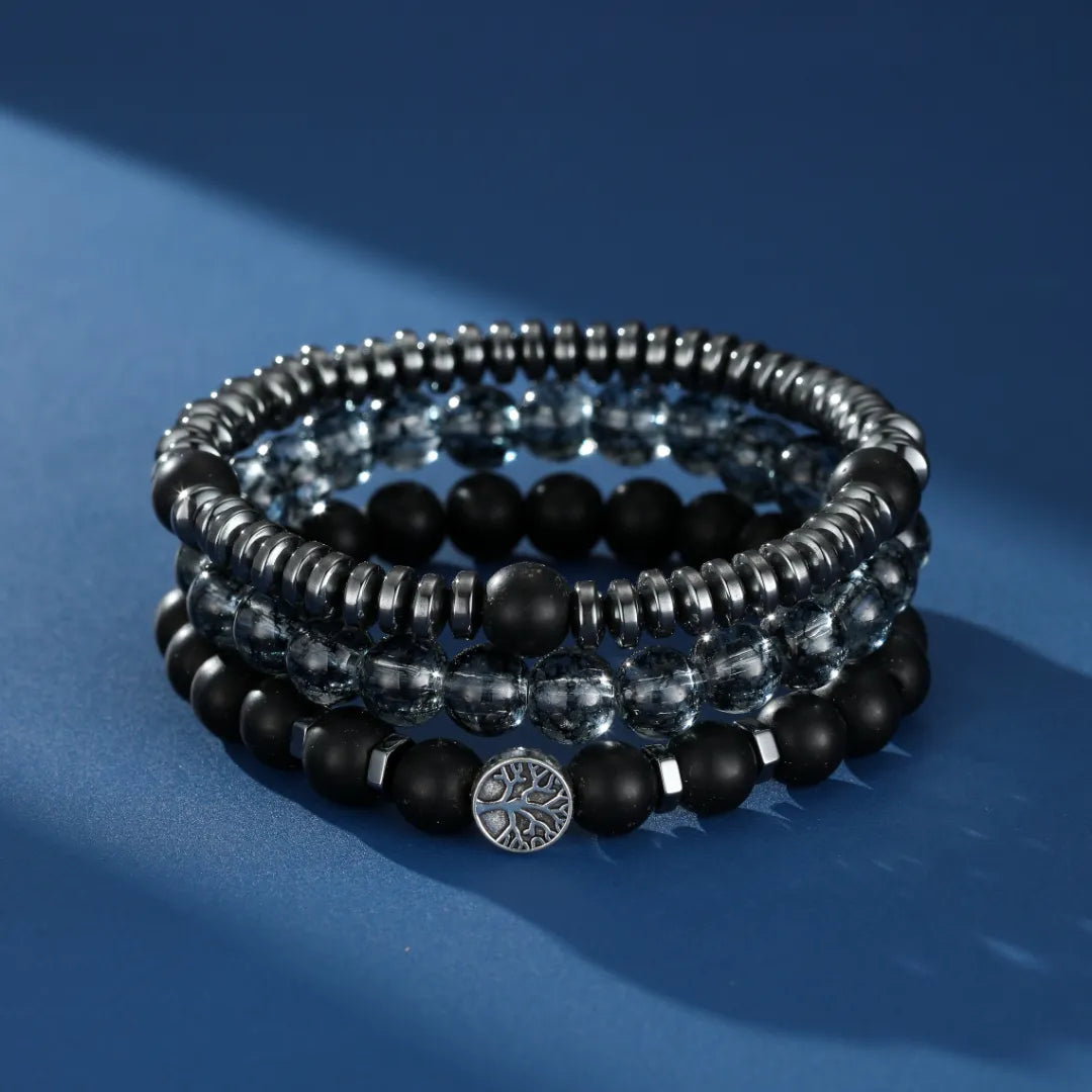 Ensemble de trois bracelets pour homme : un bracelet en hématite, un bracelet en obsidienne noire et un bracelet avec des perles transparentes et un pendentif arbre de vie argenté.