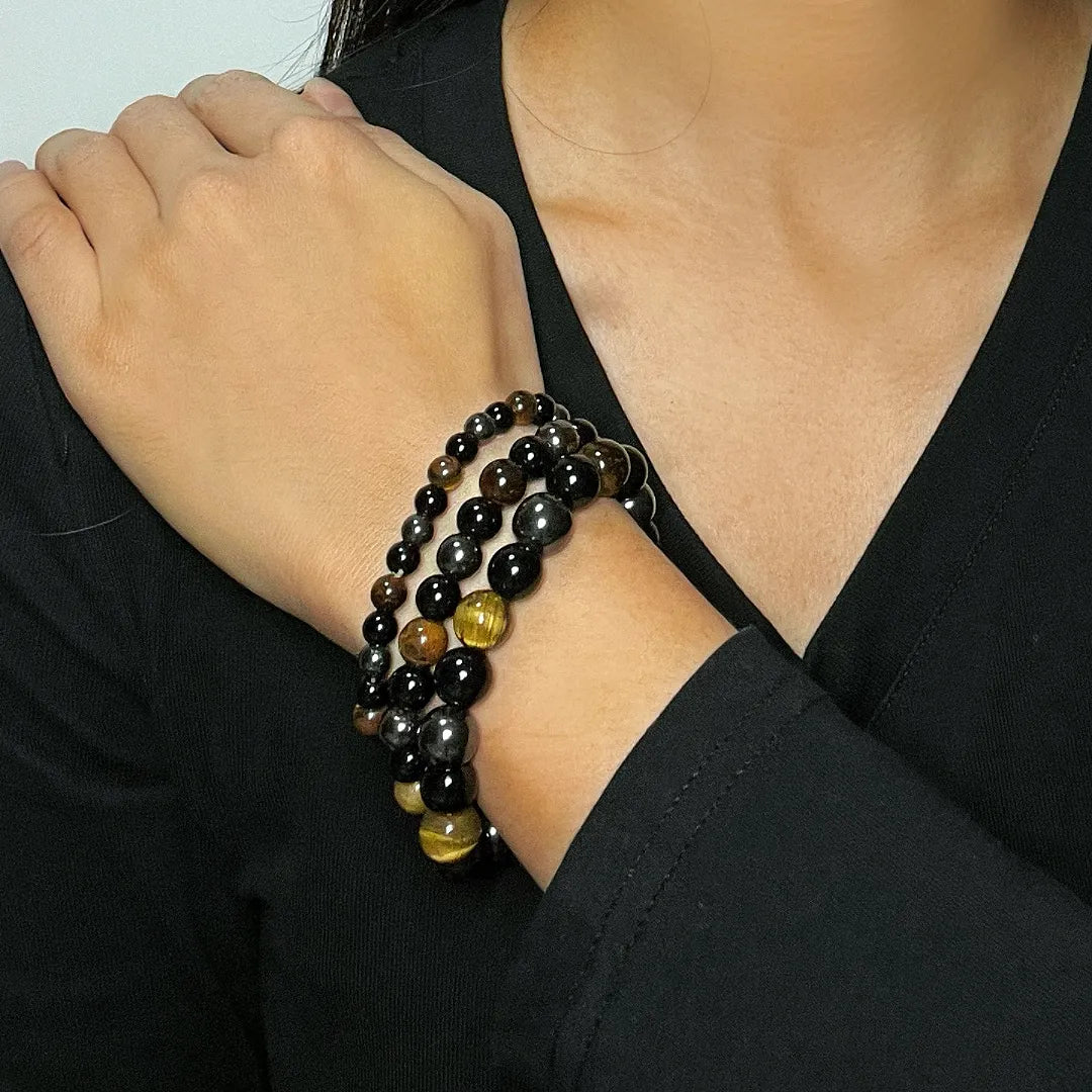 Bracelet œil de tigre et hématite 'Force Protectrice' porté au poignet, montrant les perles noires et dorées de différentes tailles.