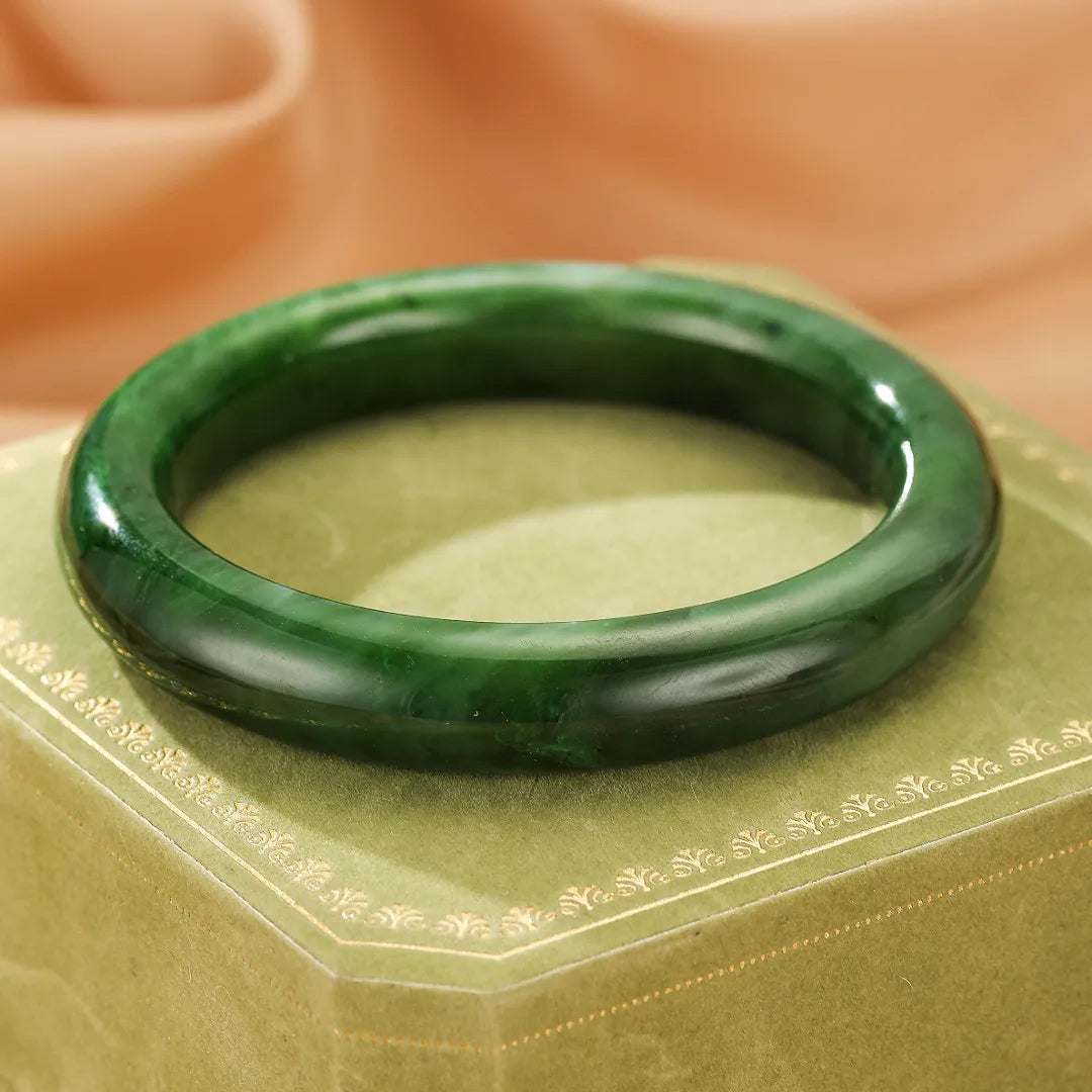 Bracelet jonc en jade "Verdure Éternelle" d'un vert profond, posé sur une boîte verte ornée de motifs dorés.