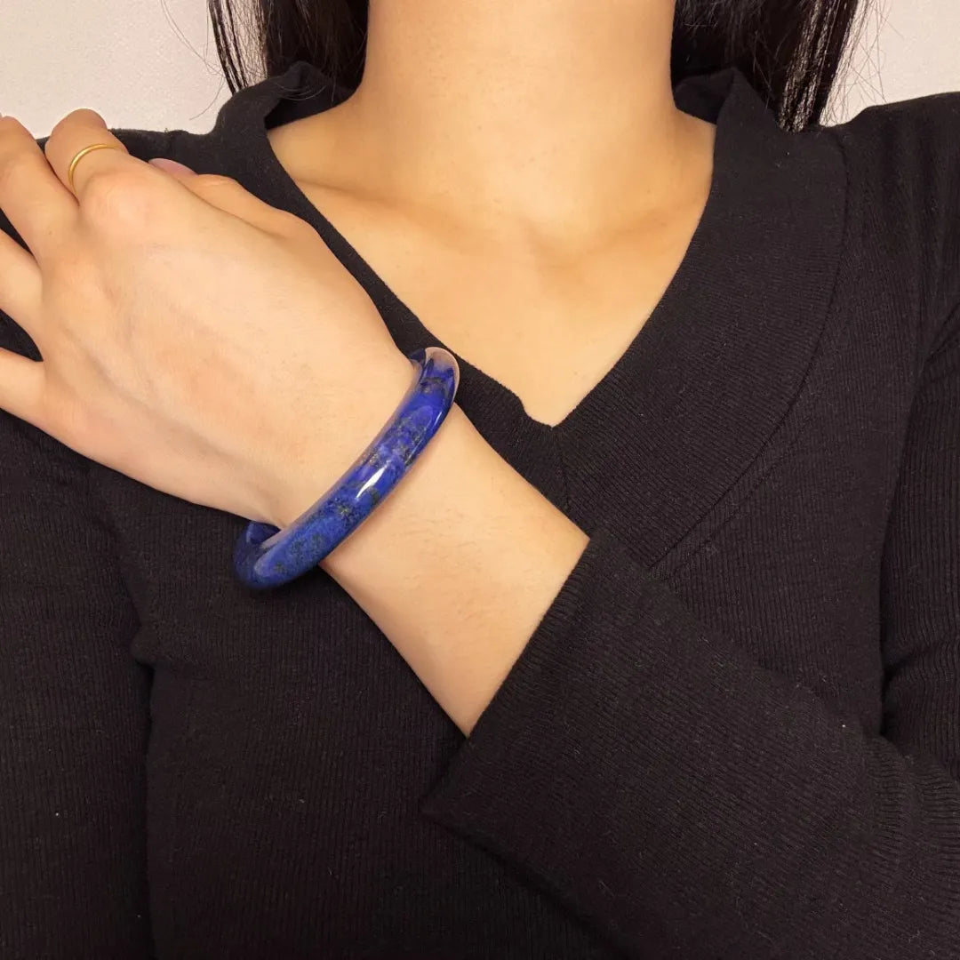 Bracelet jonc en lapis lazuli naturel, bleu profond avec inclusions dorées, porté au poignet d'une femme sur un pull noir.