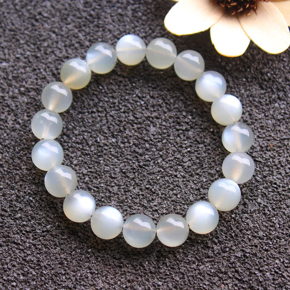 Bracelet en pierre de lune blanche aux reflets nacrés, monté sur un cordon élastique, présenté sur un fond texturé sombre.