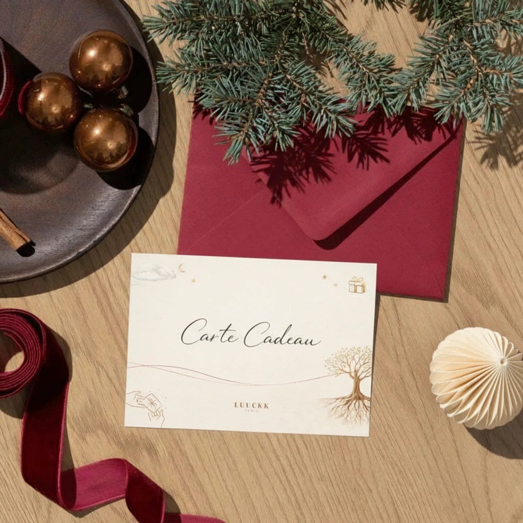 Carte cadeau Luuckk sur fond de bois, décorée de branches de sapin, d'une enveloppe rouge, de boules de Noël cuivrées et d'un ruban de velours.
