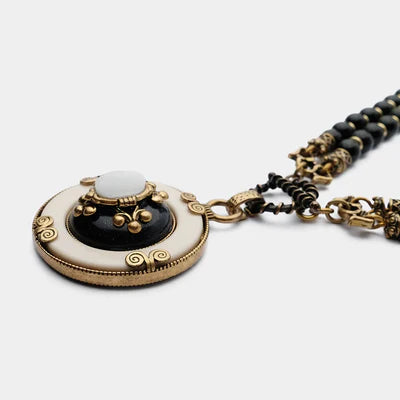 Collier "Pureté Mystique" avec pendentif rond en agate noire et blanche, bordure crème et détails dorés, monté sur une double chaîne de perles noires.