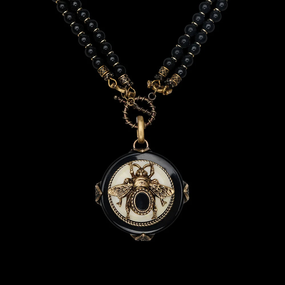 Collier "Reine Noire" en agate noire avec un pendentif rond noir et blanc orné d'une abeille dorée détaillée et d'une petite pierre noire centrale.