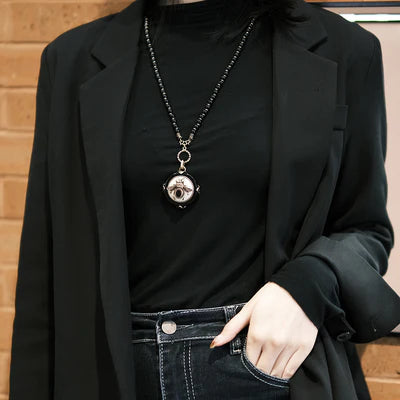 Collier Agate Noire "Reine Noire" avec un pendentif rond orné d'une abeille stylisée, porté sur un haut noir et un blazer noir.