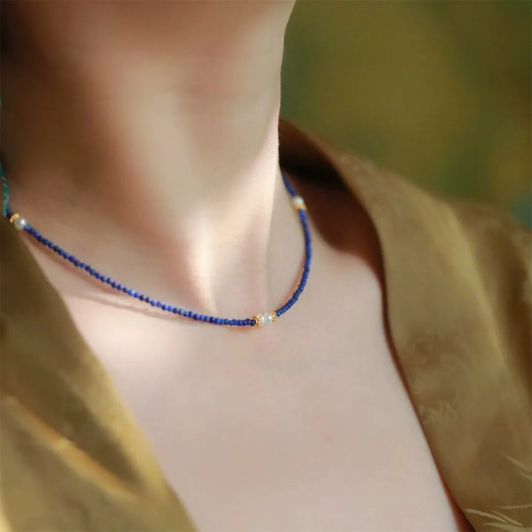 Collier Delicatesse en lapis lazuli bleu avec de petites perles blanches et des accents dorés, porté autour du cou.