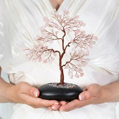 Arbre de Vie "Douceur Amoureuse" en quartz rose, tenu dans les mains d'une personne devant un tissu blanc