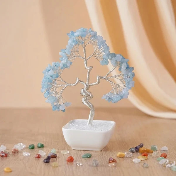 Arbre de vie décoratif en pierres bleues naturelles et fil métallique argenté, posé dans un pot blanc carré, entouré de petites pierres colorées sur un fond clair.
