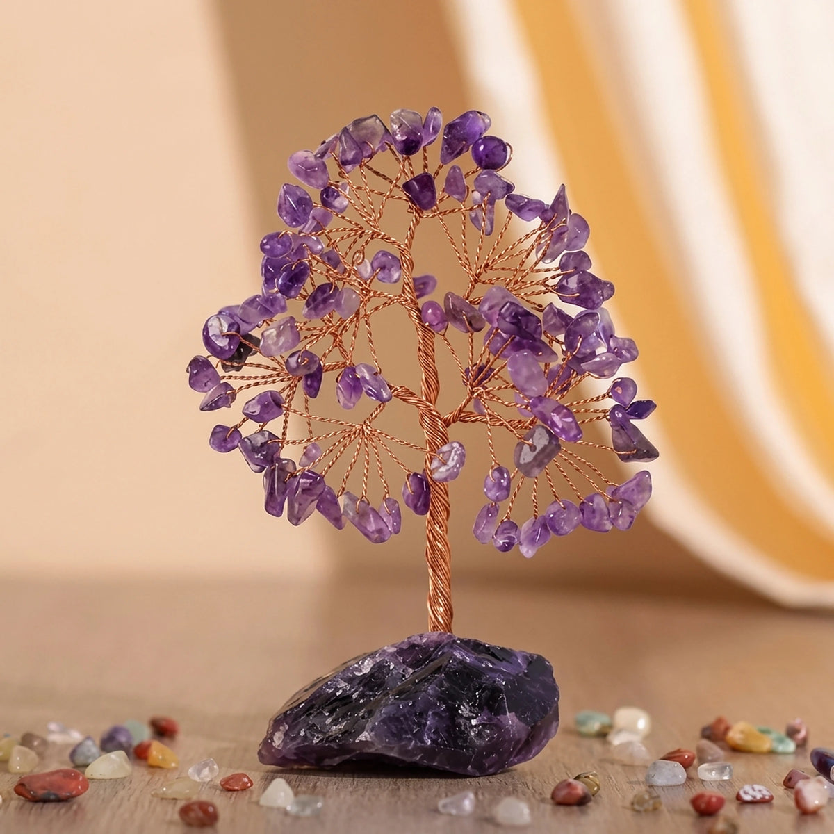 Arbre de Vie artisanal en pierres d'améthyste violettes, avec un tronc torsadé en fil de cuivre et une base en pierre d'améthyste brute, entouré de petites pierres décoratives.